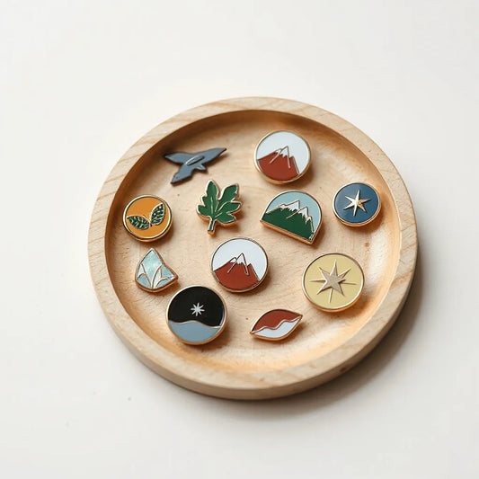 Colección de pines artesanales con diseños originales sobre una bandeja de madera clara
